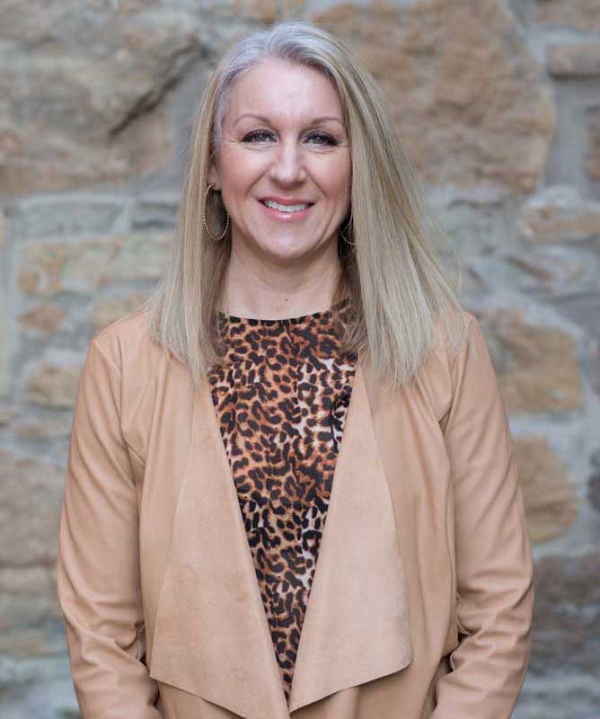 woman with long blonde hair wearing leopard print shirt in front of stone wall