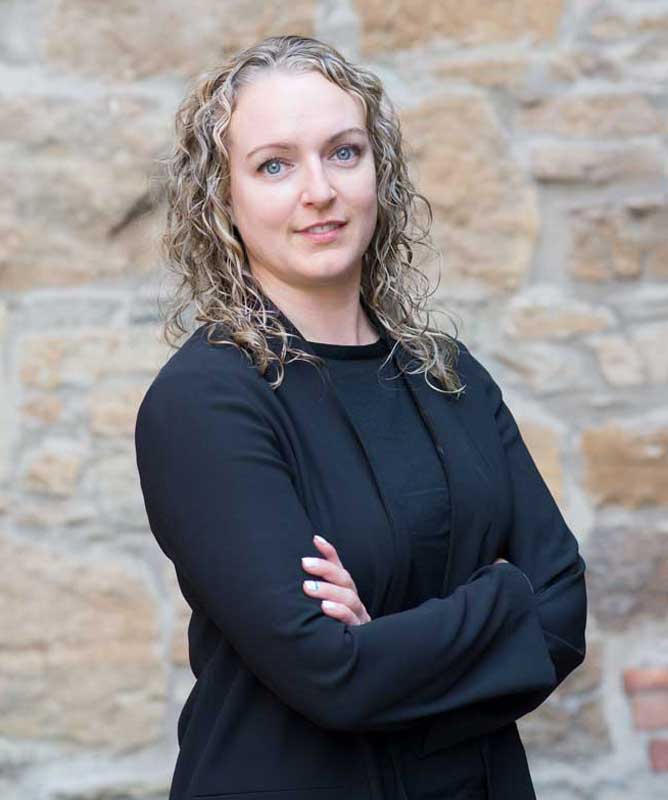 young woman with curly blonde hair wearing black shirt in front of stone wall