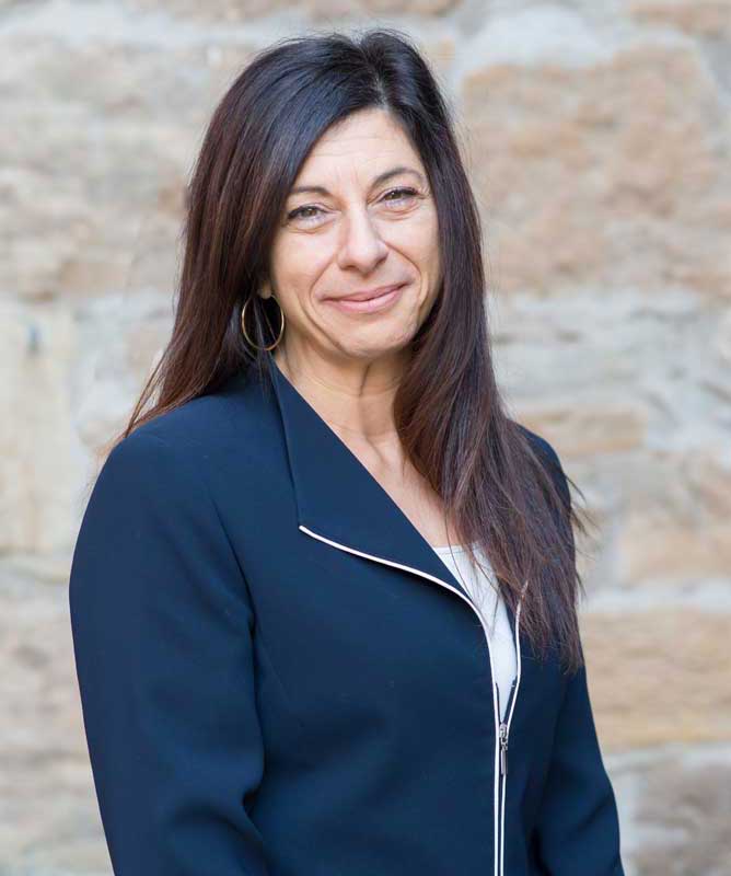 woman with long brown hair wearing navy coat in front of stone wall