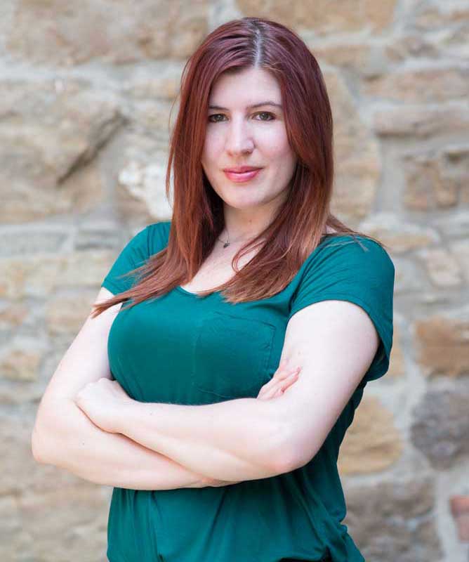 young woman with red hair wearing green t shirt with arms crossed in front of stone wall