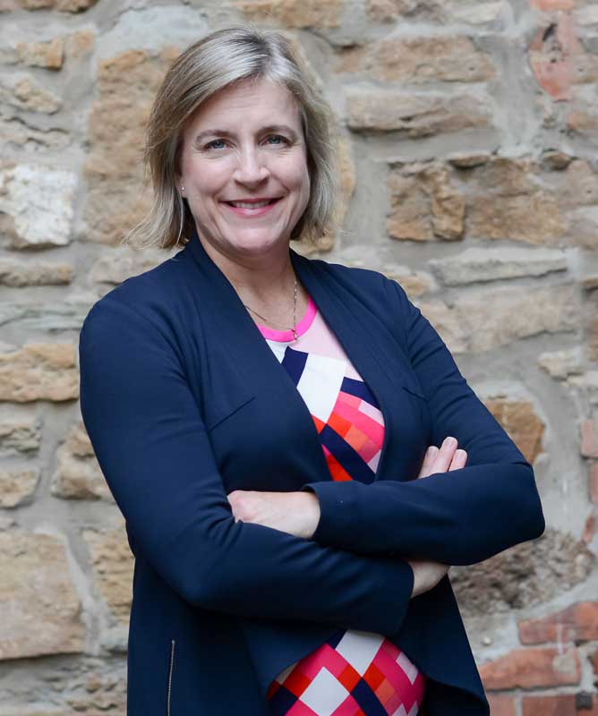 smiling woman with blond hair wearing navy blazer and colourful checkered shirt